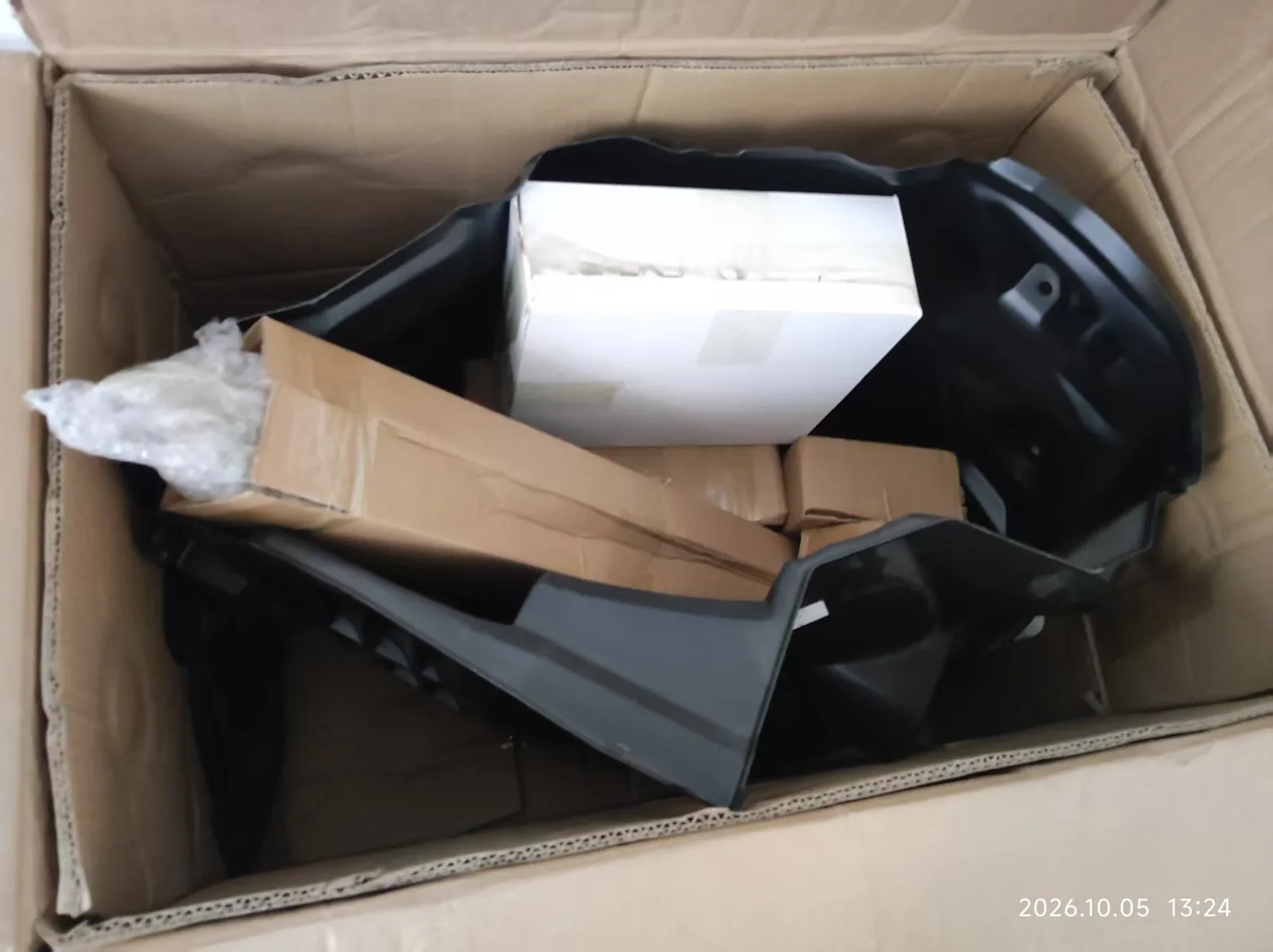 Open cardboard shipping carton containing black molded automotive parts and smaller packages